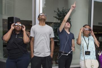 A group of students views the eclipse through eclipse glasses.