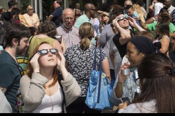 Two people in the crowd view the eclipse with eclipse glasses.