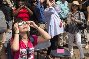 A person in the crowd views the eclipse with eclipse glasses.
