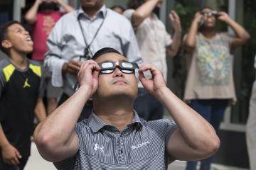 An Eclipse Party Goer views the eclipse through eclipse glasses.