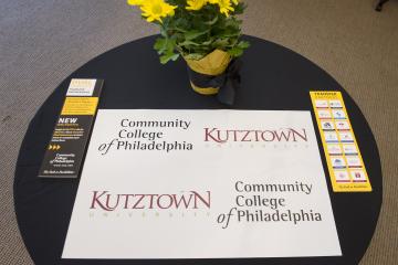 A table with signage for the Community College of Philadelphia and Kutztown University dual signing ceremony.
