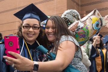 Two graduates with balloons take a selfie after the ceremony.