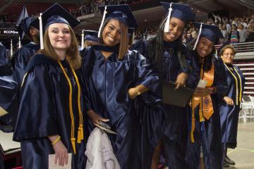 A group of graduates pose for the camera, hands on hips.