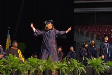 A graduate walks across the stage and raises her arms in celebration.