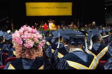 Shot of seated graduates, one wearing a mortar board decorated with pink flowers.