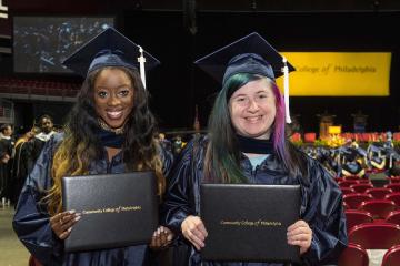 Two graduates hold up their diplomas.