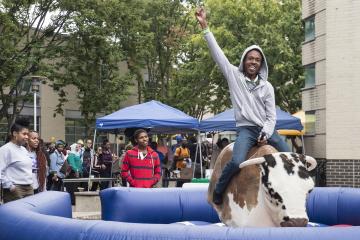 A rider raises his hand and smiles as he rides the mechanical bull.